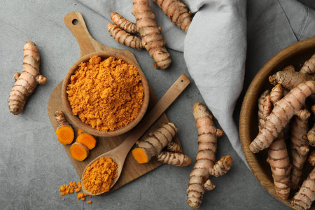 Aromatic turmeric powder and raw roots on gray table, flat lay