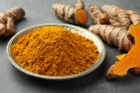 Plate with turmeric powder and raw roots on gray table, closeupの写真素材