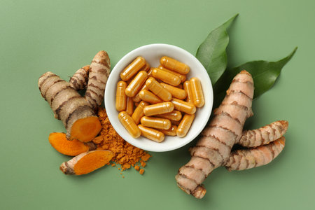 Aromatic turmeric powder, pills and raw roots on green background, flat lay