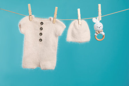Knitted baby clothes and handmade toy drying on washing line against turquoise backgroundの写真素材