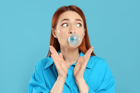 Surprised woman blowing bubble gum on turquoise backgroundの写真素材