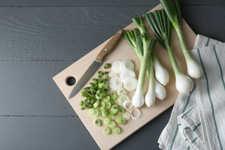 Board with knife, whole and cut spring onions on gray wooden table, flat lay. Space for textの写真素材