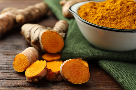 Bowl with aromatic turmeric powder and cut roots on wooden table, closeupの写真素材
