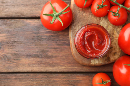 Jar of tasty ketchup and tomatoes on wooden table, flat lay. Space for textの写真素材
