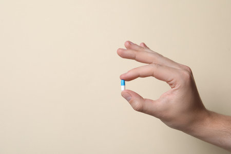 Man holding pill on beige background, closeup. Space for textの写真素材