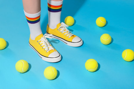 Woman wearing yellow classic old school sneakers and tennis balls on light blue background, closeupの写真素材