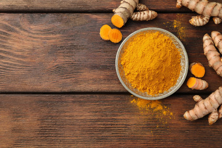 Plate with aromatic turmeric powder and cut roots on wooden table, flat lay. Space for textの写真素材