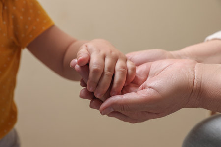 Woman holding hands with her granddaughter on beige background, closeupの写真素材