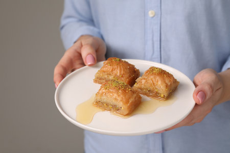 Woman with plate of delicious sweet baklava on gray background, closeupの写真素材