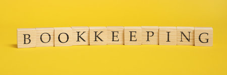 Word Bookkeeping made with wooden cubes on yellow backgroundの写真素材
