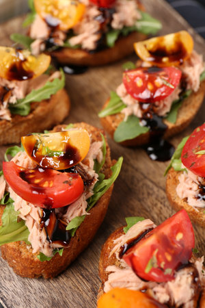 Delicious bruschettas with balsamic vinegar, tomatoes, arugula and tuna on wooden table, closeupの写真素材