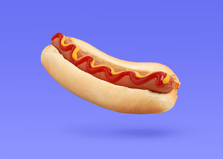 Yummy hot dog with ketchup and mustard in air against blue violet backgroundの写真素材