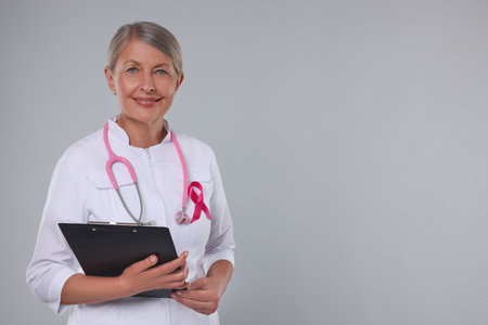 Doctor with pink ribbon, clipboard and stethoscope on light grey background, space for text. Breast cancer awarenessの写真素材
