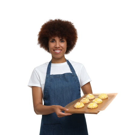 Happy young woman in apron holding board with cookies on white backgroundの写真素材