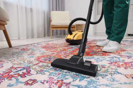 Dry cleaner's employee hoovering carpet with vacuum cleaner indoors, closeupの写真素材