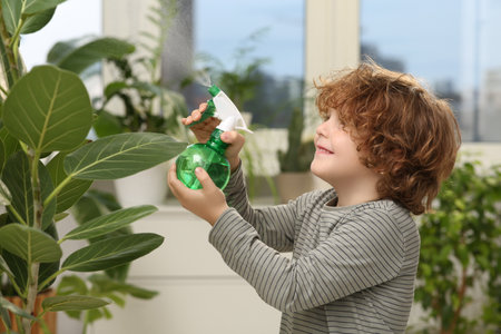Cute little boy spraying beautiful green plant at home. House decorの写真素材