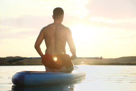 Man paddle boarding on SUP board in river at sunset, back viewの写真素材