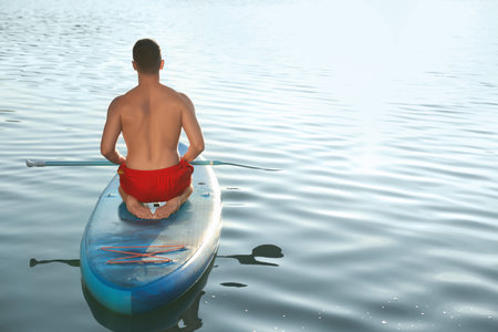 Man paddle boarding on SUP board in river at sunset, back viewの写真素材