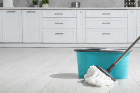Mop and bucket on white parquet in kitchen, space for text. Cleaning floorの写真素材