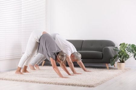 Senior couple practicing yoga on carpet at home. Healthy lifestyleの写真素材