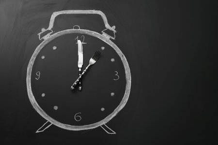Drawn alarm clock and cutlery on black surface, top view with space for text. Business lunch concept