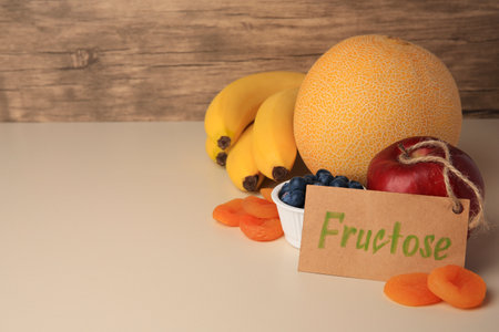 Card with word Fructose, delicious ripe fruits, blueberries and dried apricots on beige table, space...