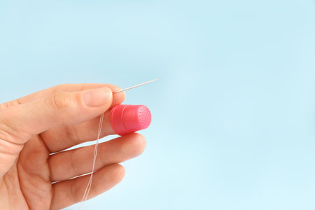 Woman with thimble, thread and sewing needle on light blue background, closeup. Space for text