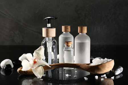Retreat concept. Bottles with cosmetic products, sea salt, spa stones and orchid flower on wet...