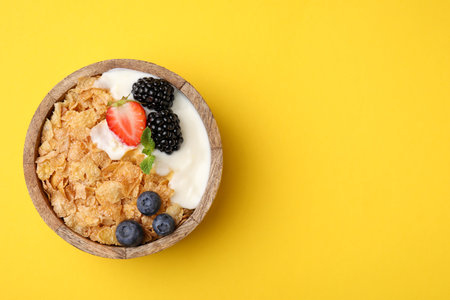 Delicious crispy cornflakes, yogurt and fresh berries in bowl on yellow background, top view with space for text. Healthy breakfastの写真素材