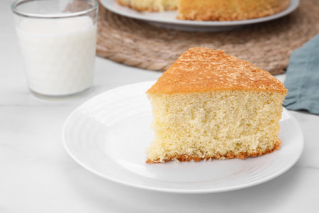 Plate with piece of tasty sponge cake on white marble tableの写真素材