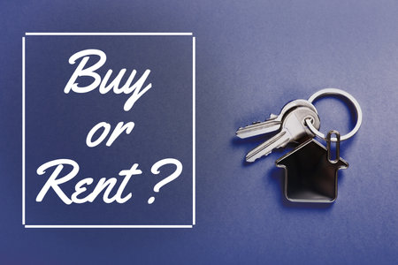 Keys with trinket in shape of house and words Buy Or Rent on blue background, top viewの写真素材