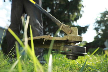 Man cutting green grass with string trimmer outdoors, closeup