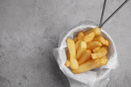 Frying basket with tasty French fries on light gray table, top view. Space for text