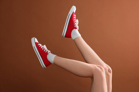 Woman wearing red classic old school sneakers on brown background, closeupの写真素材