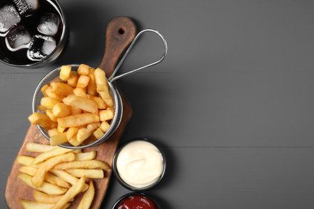 Tasty French fries, soda, ketchup and mayonnaise on gray table, flat lay. Space for textの写真素材