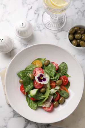 Delicious salad with vegetables and olives served on white marble table, flat layの写真素材