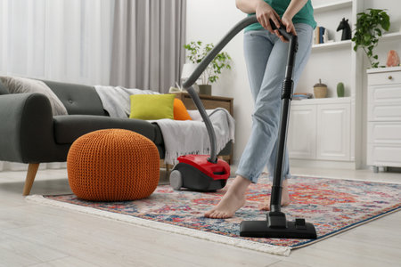 Woman cleaning carpet with vacuum cleaner at home, closeup