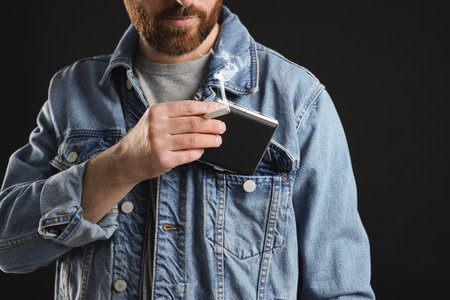 Man putting cigarette case into pocket on black background, closeup
