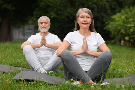 Senior couple practicing yoga on green grass in park, selective focusの写真素材