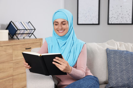 Muslim woman reading book on couch in roomの写真素材