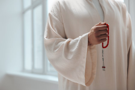 Muslim man with misbaha indoors, closeup. Space for text