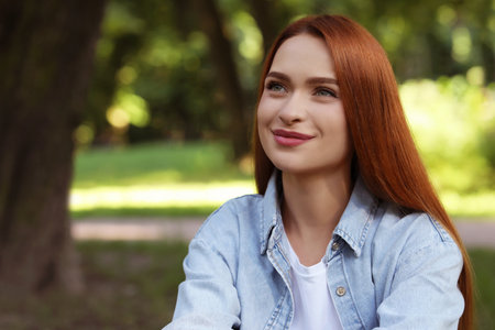 Portrait of beautiful young woman with red hair outdoors. Space for text. Attractive lady posing for...