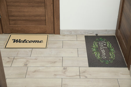 Beautiful doormats with the word Welcome on floor near doors in hallの写真素材