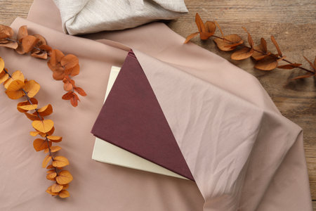 Furoshiki technique. Books, dry branches and beige fabric on wooden table, flat lay