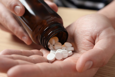 Man pouring pills from bottle at wooden table, closeupの写真素材