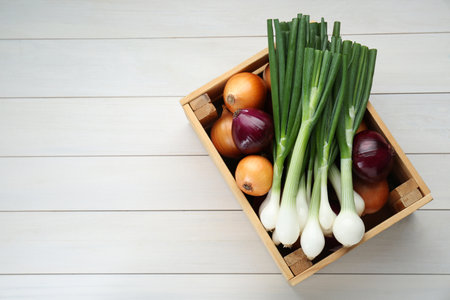 Crate with different kinds of onions on white wooden table, top view. Space for textの写真素材