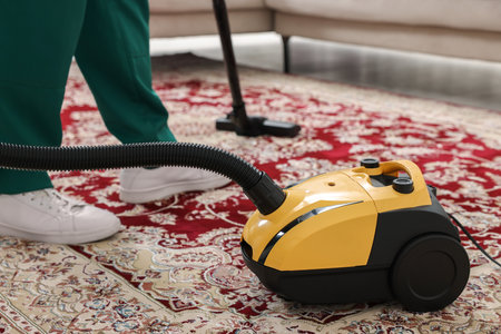 Dry cleaner's employee hoovering carpet with vacuum cleaner indoors, closeupの写真素材
