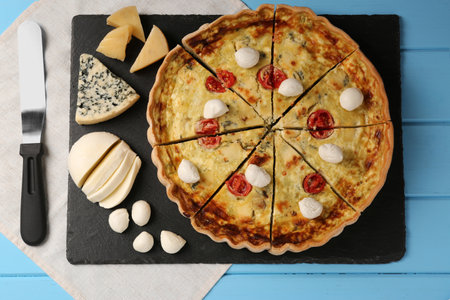 Delicious homemade cheese quiche and ingredients on light blue wooden table, flat lay