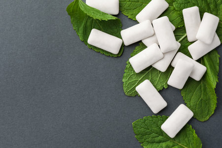Tasty white chewing gums and mint leaves on gray background, flat lay. Space for textの写真素材