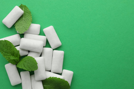 Tasty white chewing gums and mint leaves on green background, top view. Space for textの写真素材